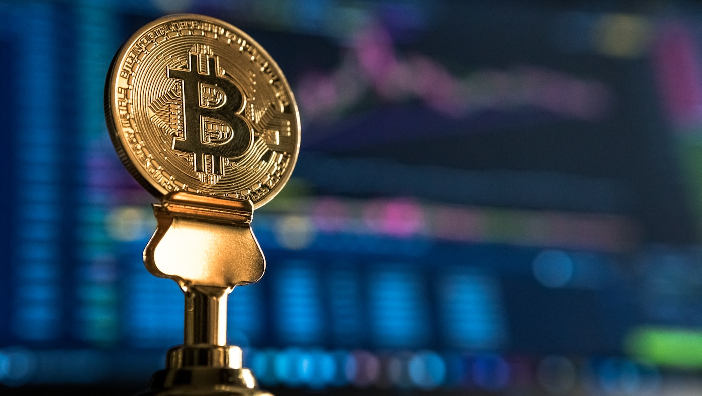 Une pièce Bitcoin sur un support devant un graphique de marché