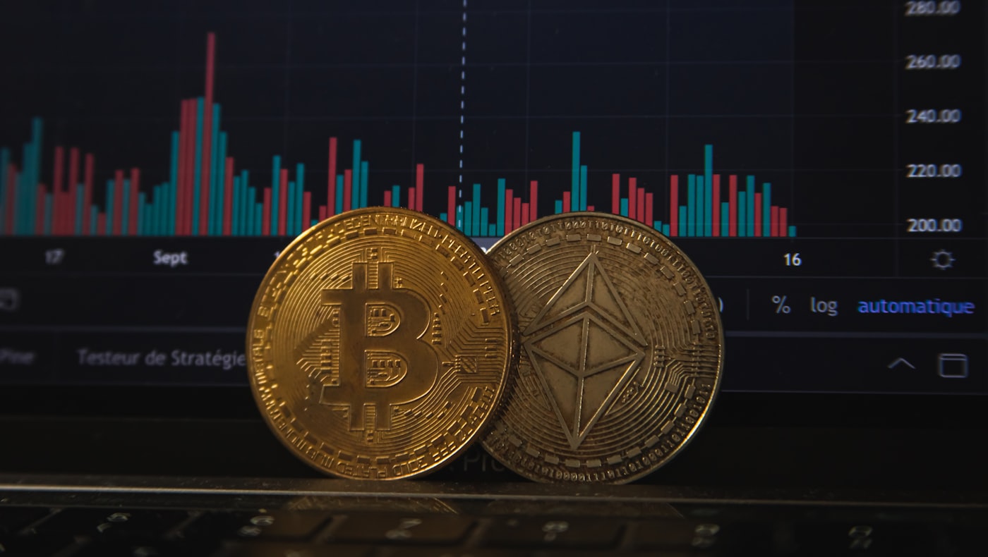 Une pièce Bitcoin et une pièce Ethereum posées sur un graphique de prix